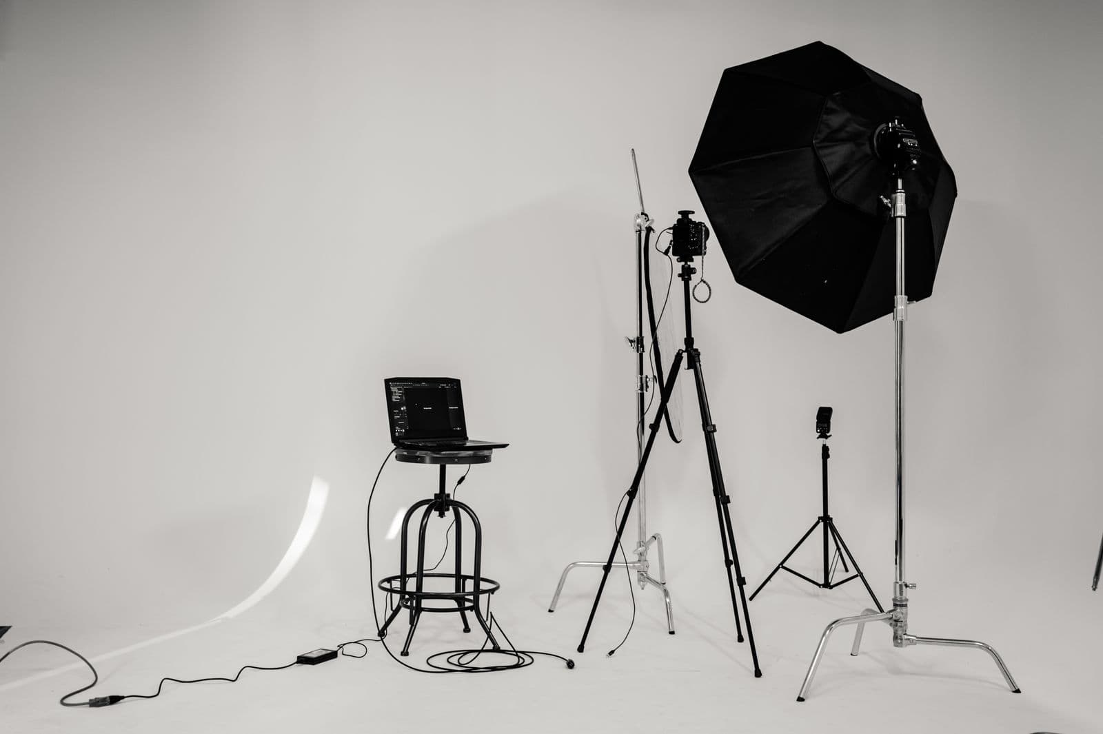 A lit studio set in black and white: octabox, tripods and a tethered laptop on a white cyclorama.